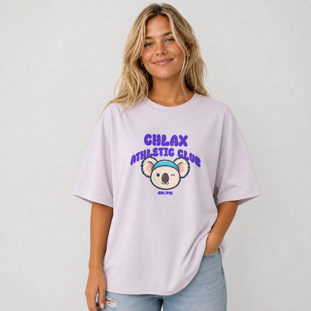 A woman wearing a light purple oversized t-shirt with a cartoon koala graphic and the text 'CHLAX ATHLETIC CLUB' on the back, paired with light blue jeans against a plain white background.