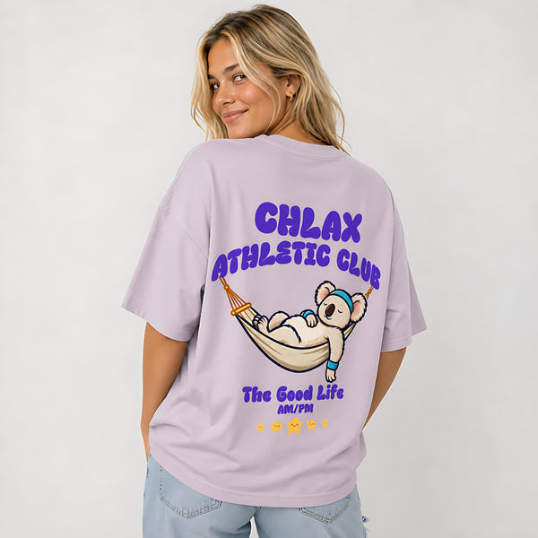 A woman wearing a light purple oversized t-shirt with a cartoon koala graphic and the text 'CHLAX ATHLETIC CLUB' on the back, paired with light blue jeans against a plain white background.
