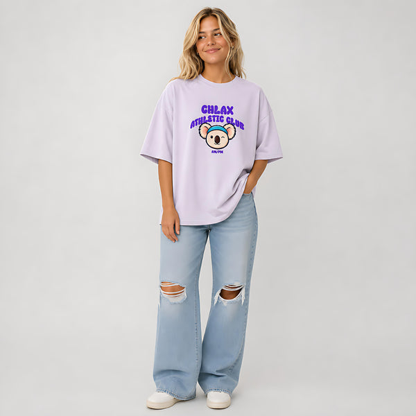 A woman modeling a light purple t-shirt with a 'CHLAX ATHLETIC CLUB' graphic featuring a cartoon koala, paired with light-wash ripped jeans and white sneakers, against a light gray studio background.