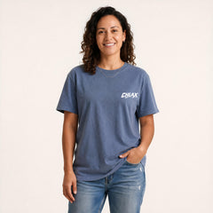 A woman wearing a blue crewneck t-shirt with a white 'CHLAX' logo on the left chest, paired with blue jeans, standing against a plain off-white background.