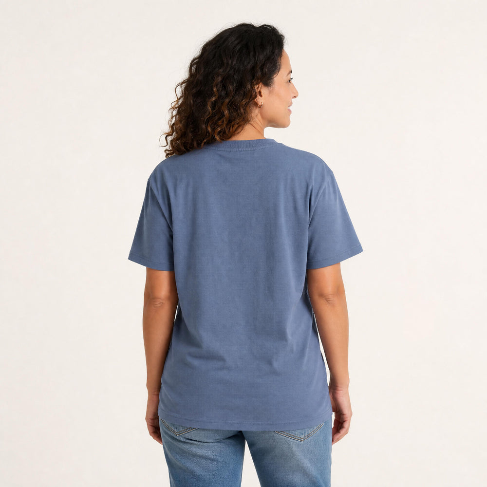 A woman wearing a blue crewneck t-shirt with a white 'CHLAX' logo on the left chest, paired with blue jeans, standing against a plain off-white background.