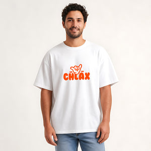 A man wearing a white crewneck t-shirt with an orange graphic that reads 'shoo shoo CHLAX' with a hand gesture, paired with blue jeans, against a plain off-white background.