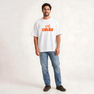 A man wearing a white short-sleeve t-shirt with an orange 'CHLAX' logo on the chest, paired with blue jeans and brown shoes, standing against a light off-white studio background.