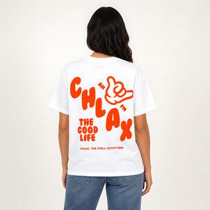 A woman viewed from the back wearing a white short-sleeve T-shirt with a large orange graphic print on the back that reads 'I'M CHLAX THE GOOD LIFE' and 'CHLAX, THE CHILL OUTFITTERS,' paired with blue jeans against a plain light background.