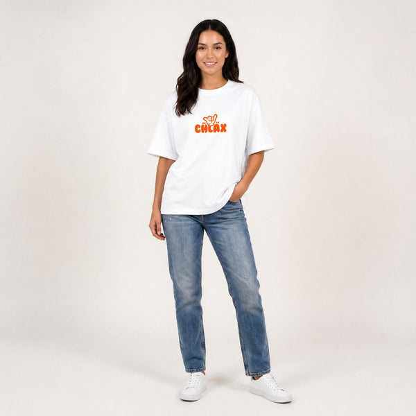 A woman modelling a white crewneck t-shirt with a bold orange 'CHLAX' graphic on the chest, paired with blue jeans and white sneakers, against a plain light beige studio background.
