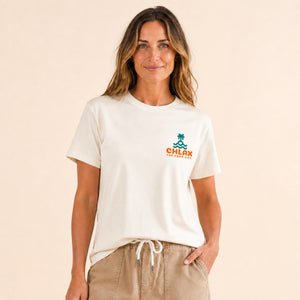 A woman wearing a cream-colored short-sleeve t-shirt with a small green and orange 'CHLAX' logo on the left chest, paired with khaki drawstring pants, against a solid beige background.