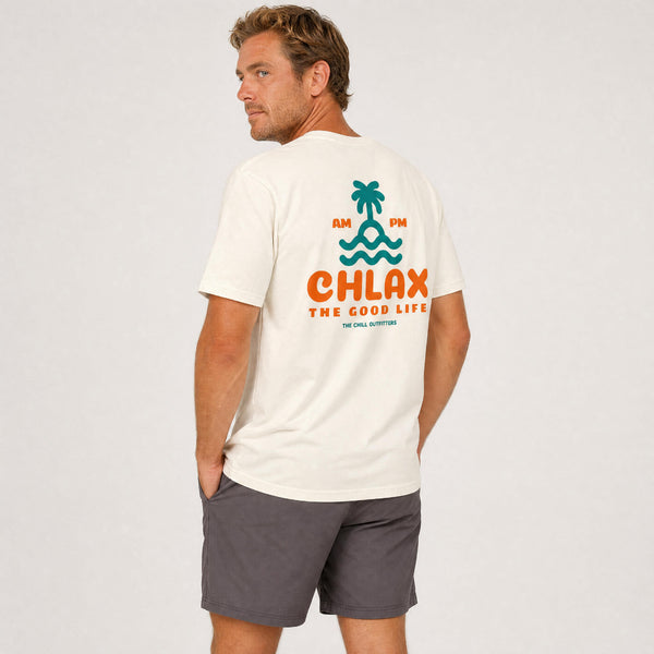 A man wearing a cream-colored t-shirt with a green and orange back graphic that reads 'CHLAX THE GOOD LIFE' and 'AM PM', paired with dark gray shorts, photographed against a light gray studio background.