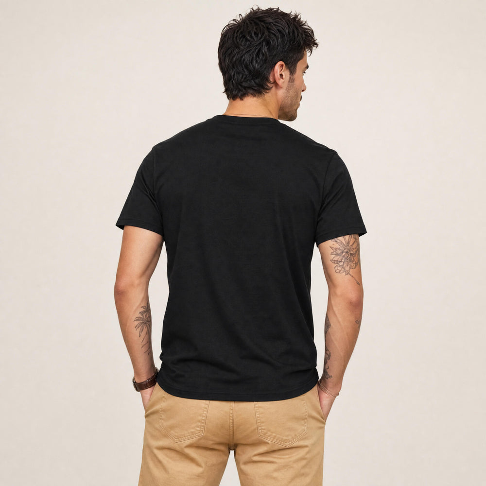 A man wearing a black crewneck t-shirt with a white 'Chlax' logo on the left chest, paired with khaki pants, standing against a neutral beige background.