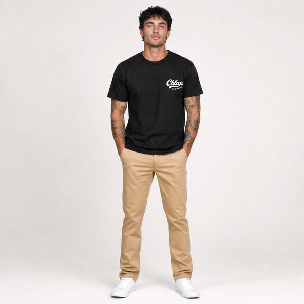 A man modeling a black crewneck t-shirt with a white 'Chlax' logo on the left chest, paired with tan pants and white sneakers, standing against a light gray studio background.