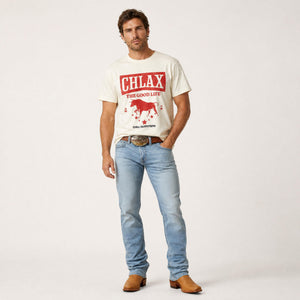 A man modeling a cream-colored graphic t-shirt with a red 'CHLAX THE GOOD LIFE' logo and horse design, paired with light blue jeans and brown cowboy boots against a plain white studio background.