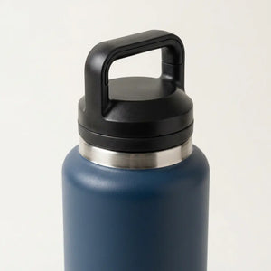 A close-up of a matte blue insulated water bottle with a black carrying handle lid and a stainless steel collar, set against a plain light background.