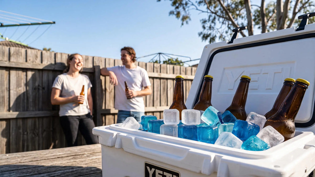A white YETI cooler filled with ice and blue bottles in an outdoor backyard setting, with two people standing behind it holding beer bottles.
