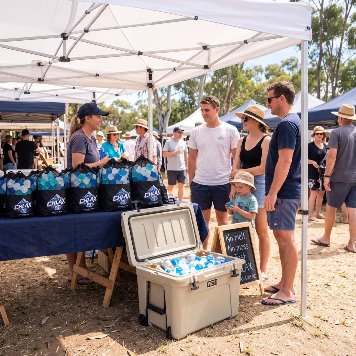 Outdoor event scene under a white canopy with people gathered around a table displaying black CHLAX branded cooler bags and an open cooler filled with bottled drinks. Several people are standing and interacting near the setup.