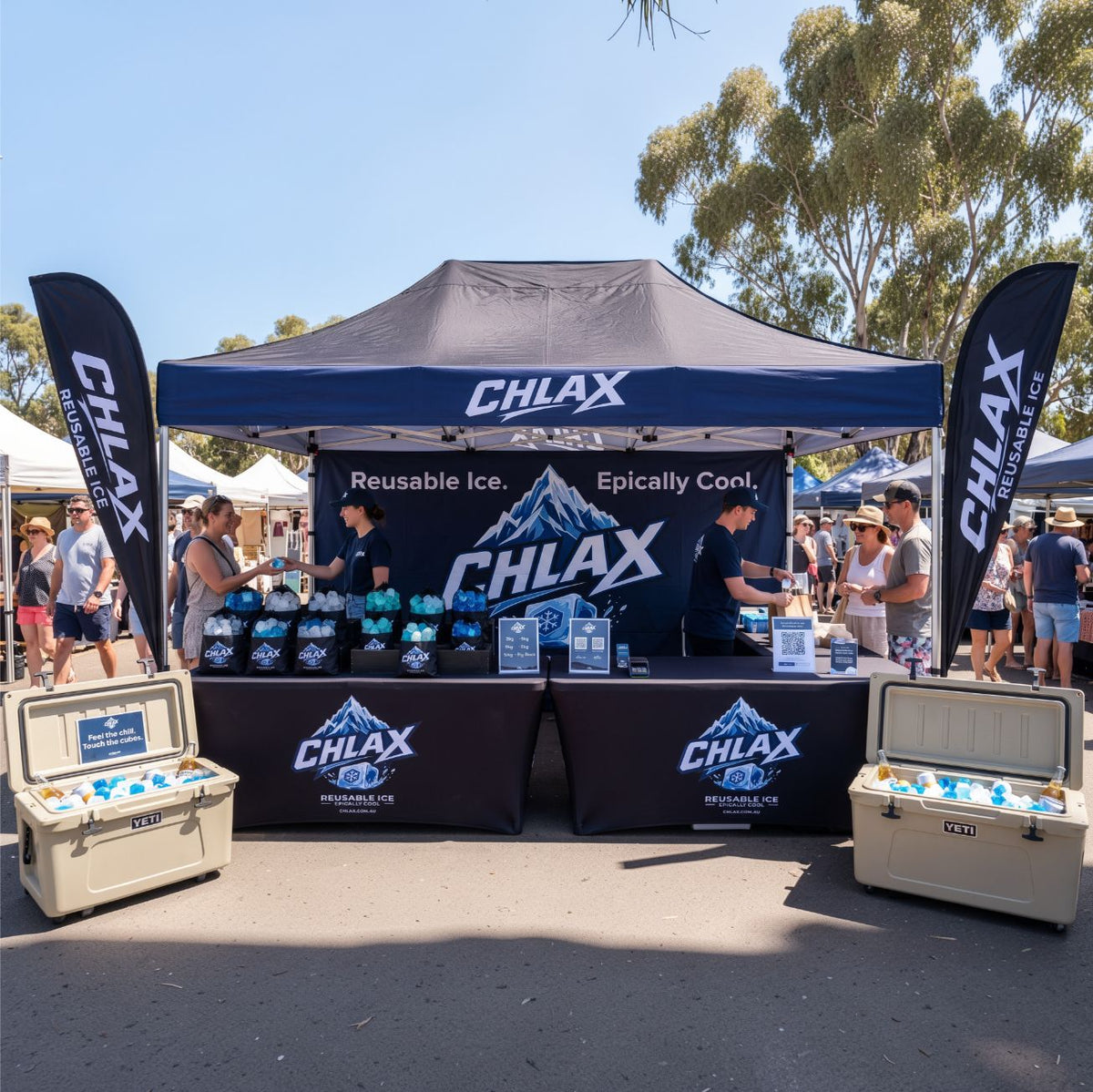A CHLAX outdoor event booth at a market or festival, with a black canopy tent, branded backdrop, two black feather flags, branded table covers, and open coolers filled with reusable ice packs on the ground.