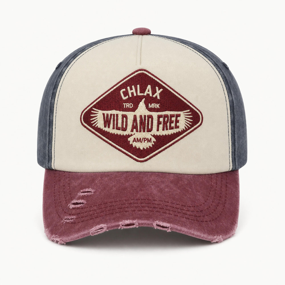 A distressed trucker-style baseball cap with a cream front panel, dark blue-gray side panels, and a faded burgundy brim. The front features a diamond-shaped embroidered patch with the text 'CHLAX TRK MK WILD AND FREE'.