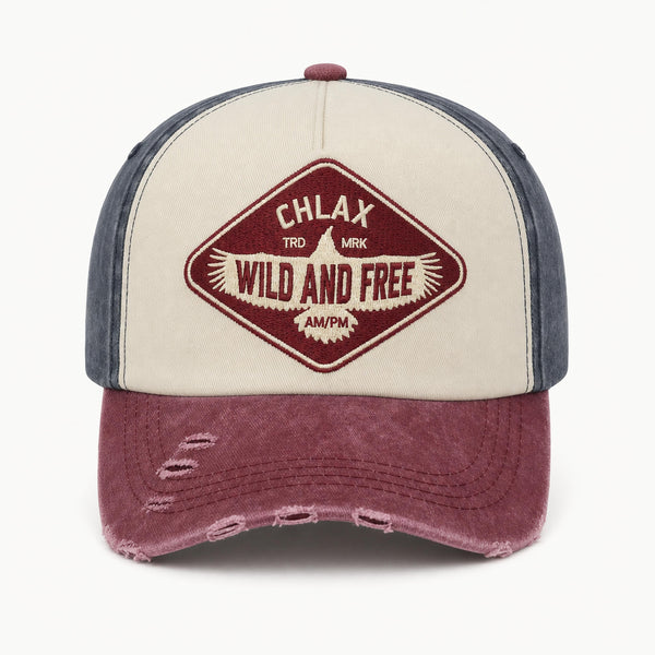A distressed trucker-style baseball cap with a cream front panel, dark blue-gray side panels, and a washed burgundy brim. The front features a diamond-shaped embroidered patch with the text 'CHLAX', 'WILD AND FREE', and 'AMPM'.