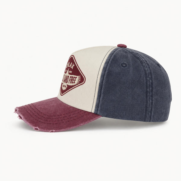 A three-panel baseball cap with a washed cream front panel, dark blue denim-style side panels, and a distressed maroon brim. A maroon diamond-shaped patch on the front reads 'CHLAX WILD AND FREE'.