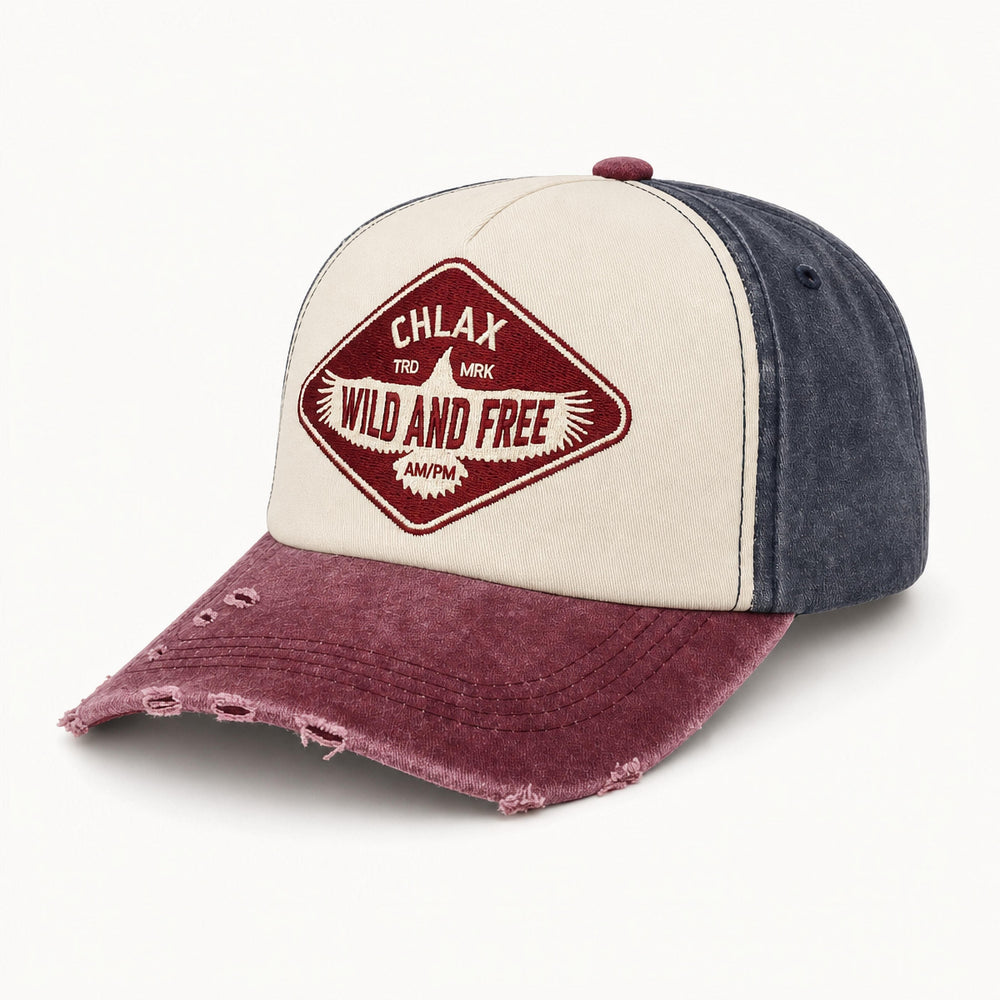 A distressed trucker-style baseball cap with a cream front panel, dark blue-gray side panels, and a faded burgundy brim. The front features a diamond-shaped embroidered patch with the text 'CHLAX TRK MK WILD AND FREE'.
