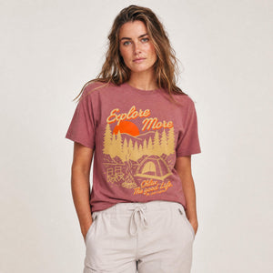 A woman modeling a dusty rose short-sleeve graphic t-shirt with a yellow and orange camping design that reads 'Explore More' and 'CHLAX The Good Life'.