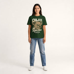 A woman modeling a dark green graphic t-shirt with a distressed beige print that reads 'CHLAX' and 'All Week Long The Good Life', paired with blue jeans and white sneakers, against a plain light background.