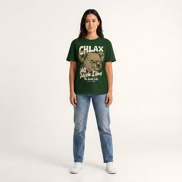 A woman modeling a dark green graphic t-shirt with a distressed beige print that reads 'CHLAX' and 'All Week Long The Good Life', paired with blue jeans and white sneakers, against a plain light background.