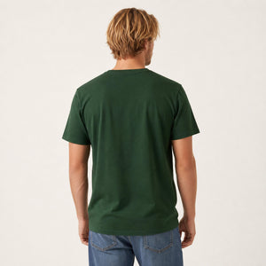 A man viewed from behind wearing a dark green short-sleeve crewneck t-shirt and blue jeans, standing against a plain off-white studio background.