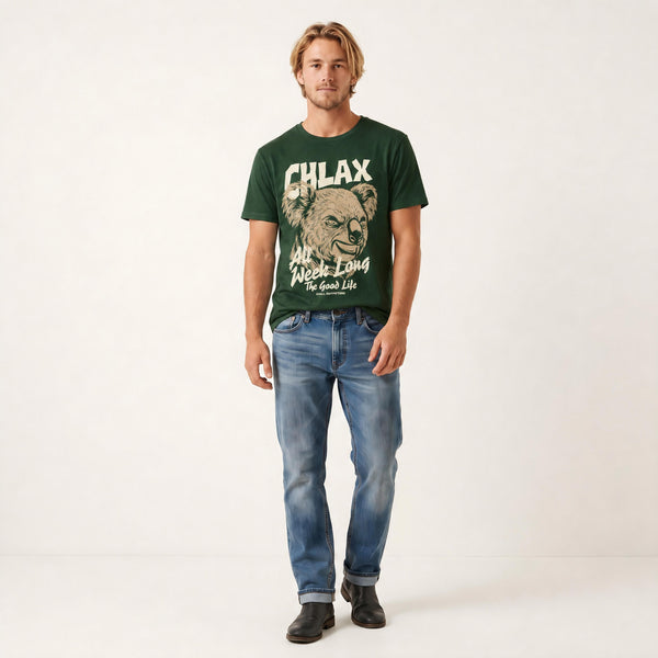 A man modeling a dark green graphic t-shirt with a bear illustration and the text 'CHLAX' and 'All Week Long The Good Life', paired with blue jeans and black shoes, against a plain white studio background.