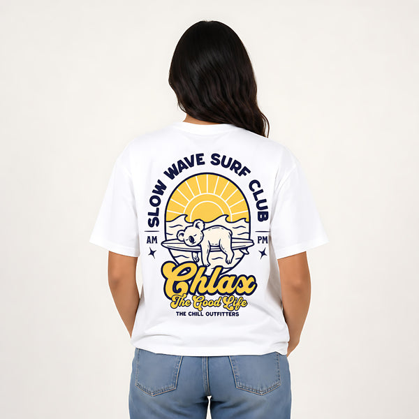 A woman viewed from the back wearing a white graphic T-shirt with a large surf-themed print and blue jeans, against a plain light background.
