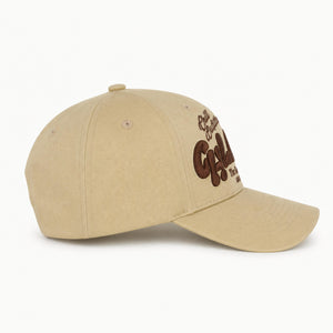 A beige baseball cap with brown embroidered text on the side, photographed on a clean white background.