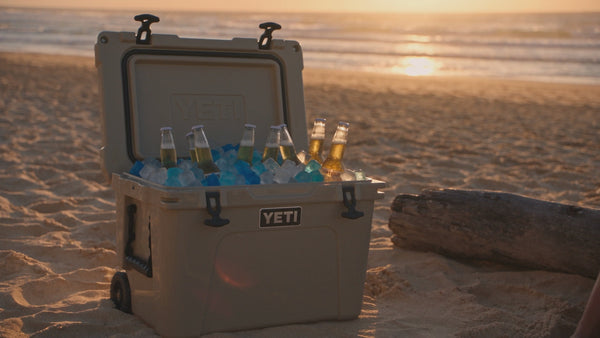 Australian beach at dusk with a Yeti cooler full of beer & CHLAX reusable ice cubes showing a young couple sitting on a log drinking beer.